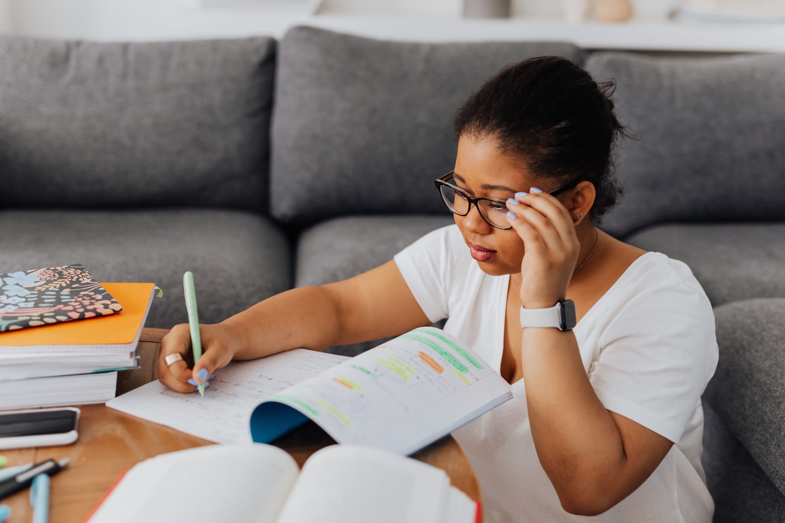 A young woman wearing glasses studies with a notebook on a table indoors, highlighting focus and learning.