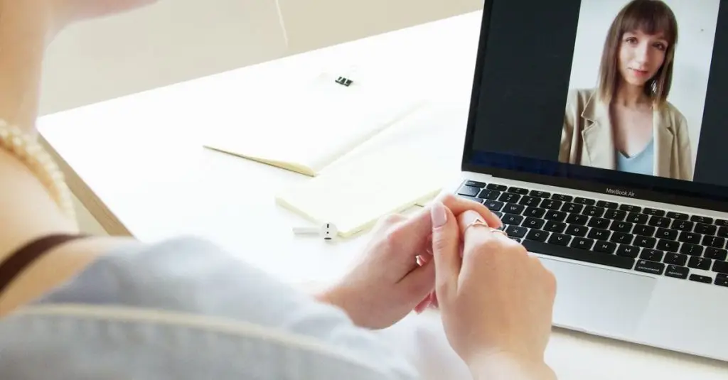 A young woman using earpods for a video call on a laptop indoors.