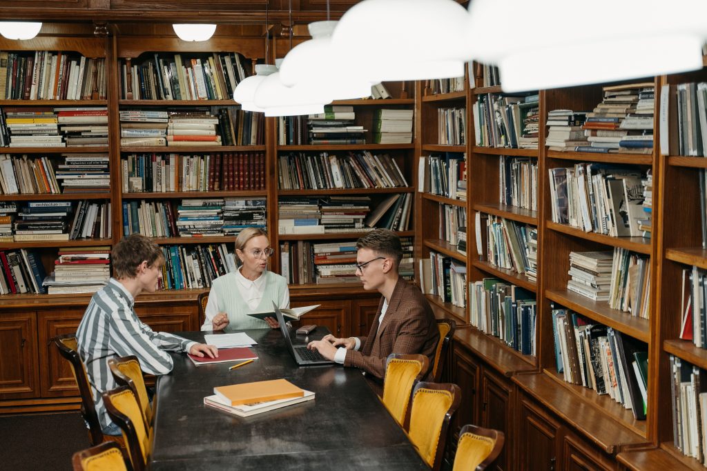 Three professionals having a meeting with laptops and documents in a well-stocked library.